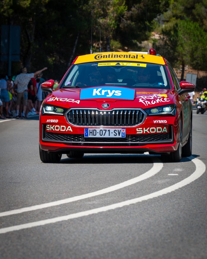 Red Skoda car participating in the Tour de France, captured outdoors during the day.