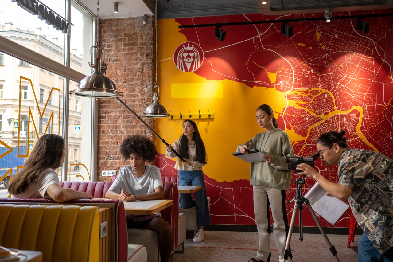 Group of young filmmakers working indoors in a vibrant restaurant setting with diverse crew members.